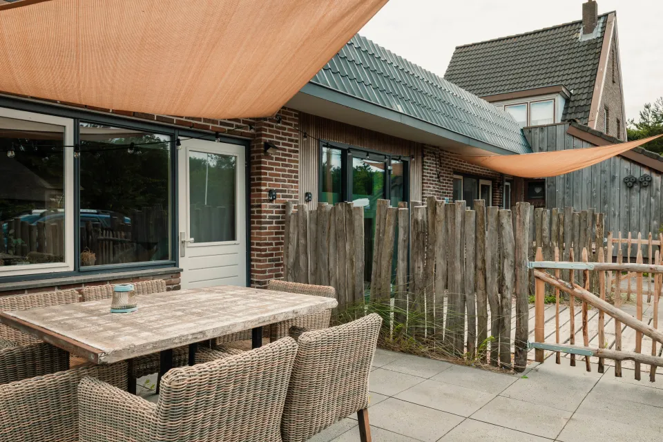 Terras met houten tafel en rieten stoelen voor de grote raampartij
