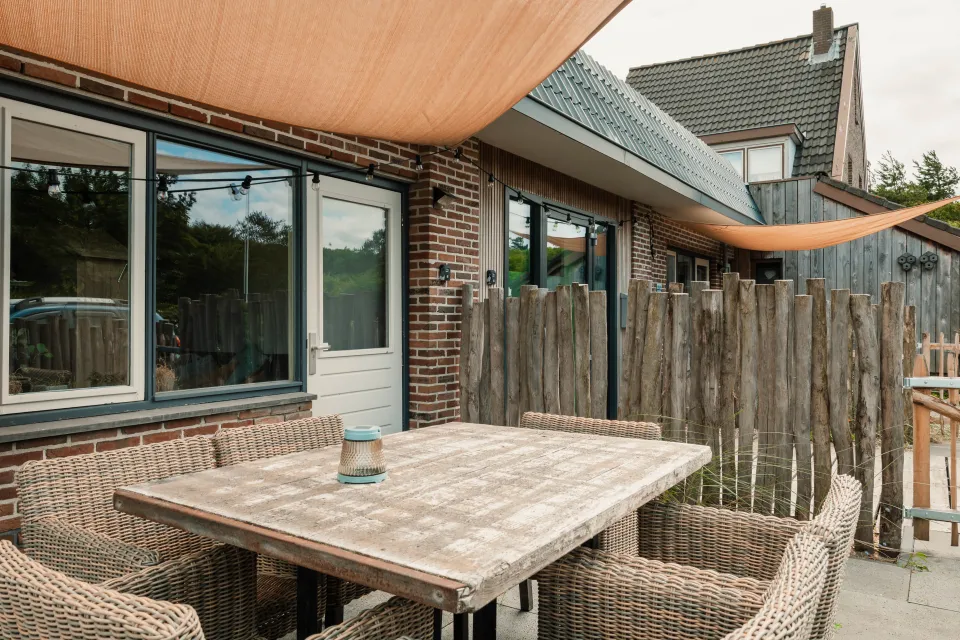 Houten tafel met rieten stoelen op het terras onder het oranje schaduwdoek