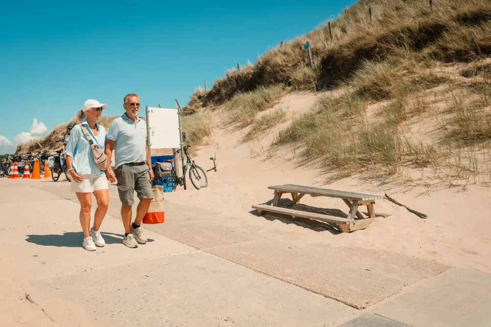 Stel loopt met tassen over de duinovergang naar het strand