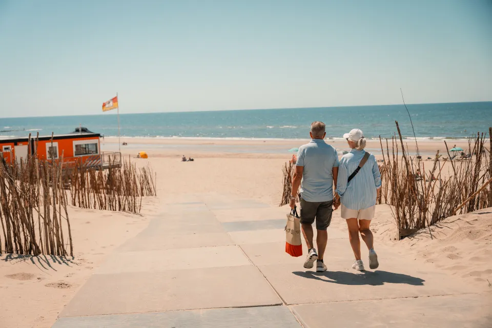 Stel loopt over het strand langs de rieten schermen richting zee
