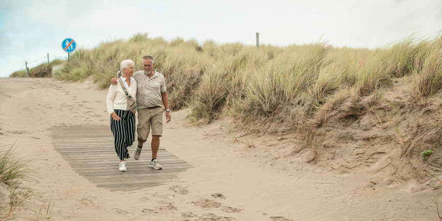 Older couple walking along a sandy path through the dunes to the beach