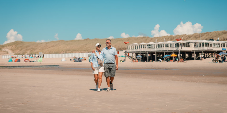 Couple walking on the beach with beach pavilions at the foot of the dune